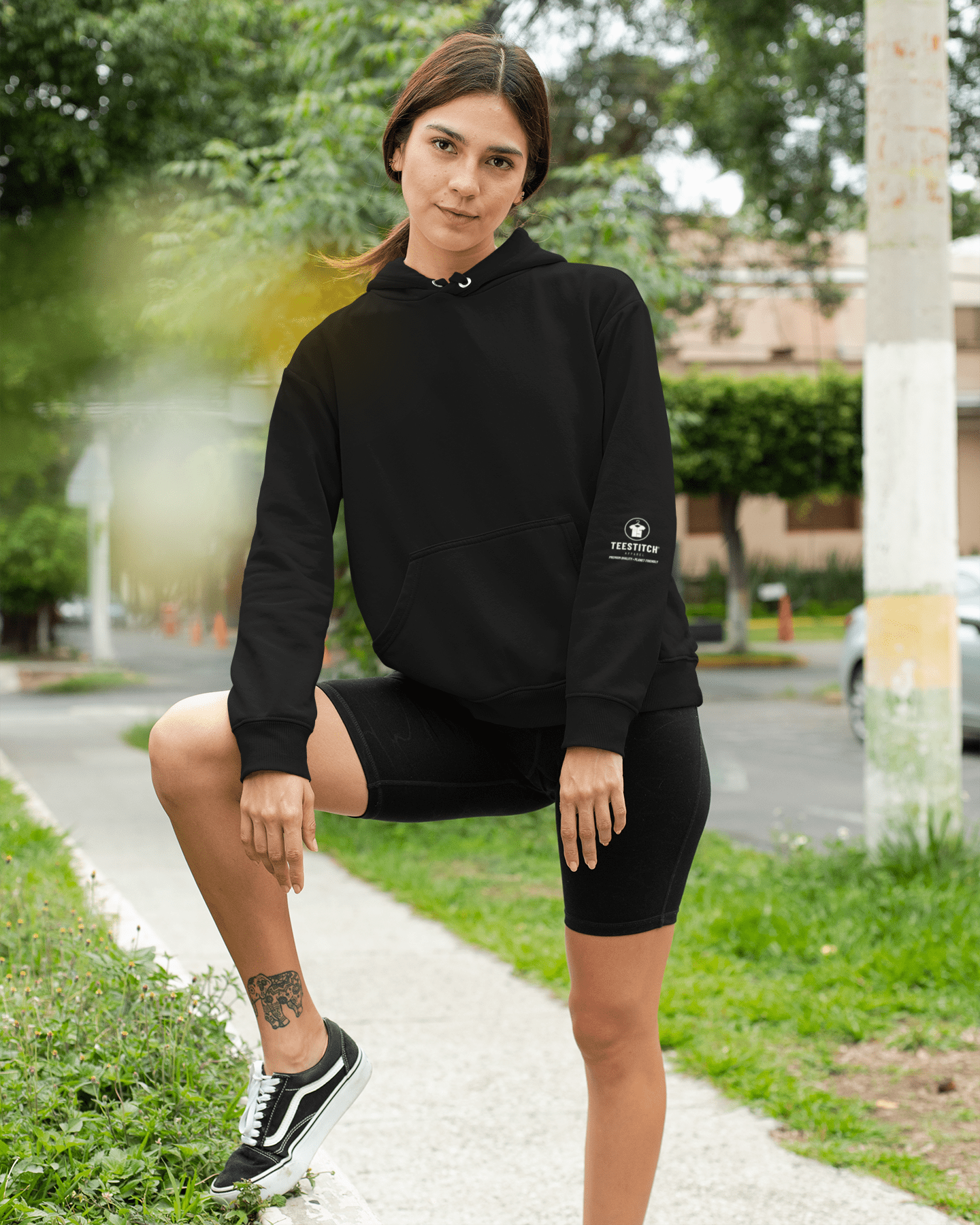 TeeStitch-Apparel-Core-Essentials-pullover-hoodie-mockup-of-a-woman-by-a-garden-street