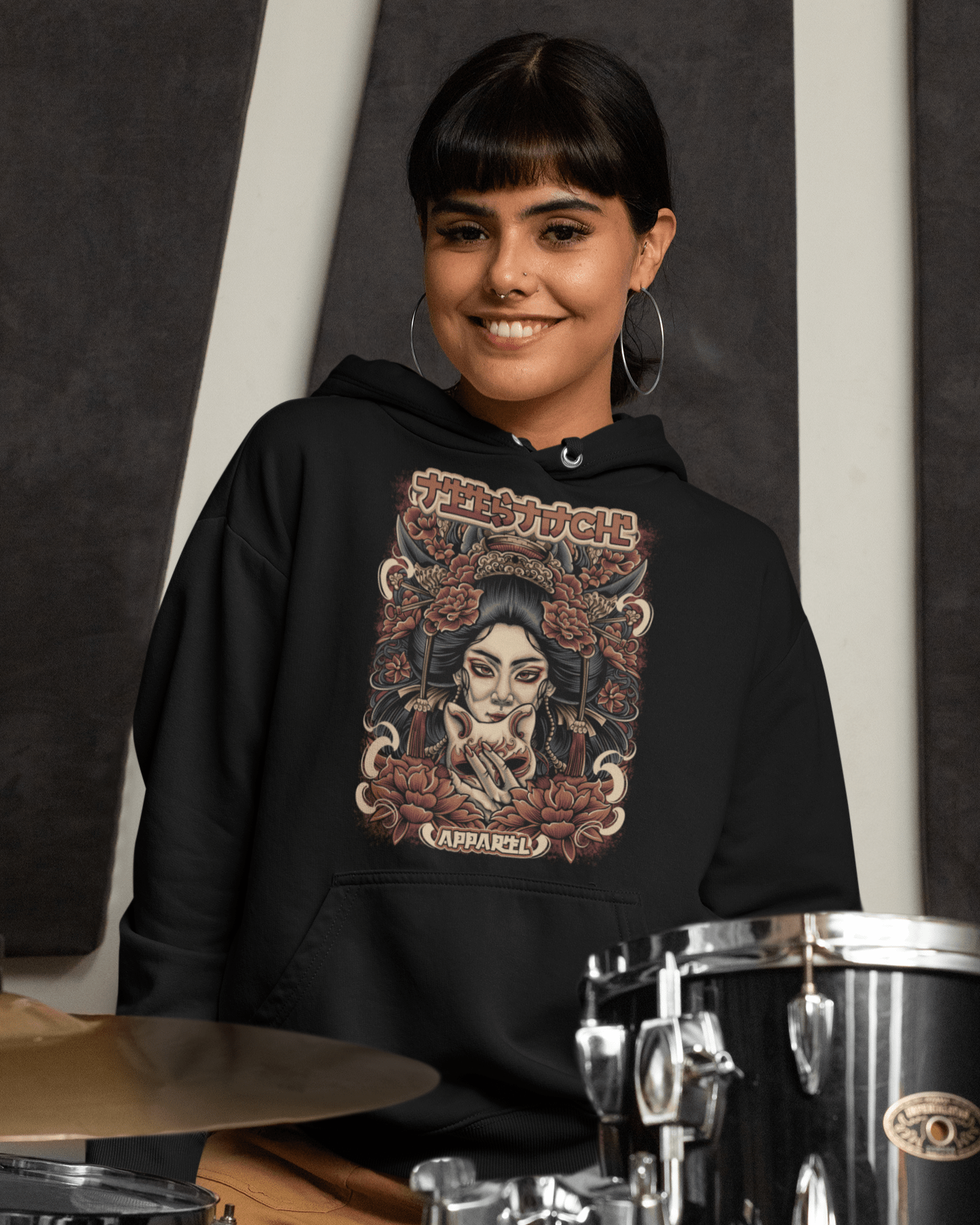 Geisha-Mask-design-pullover-hoodie-mockup-featuring-a-smiling-female-drummer