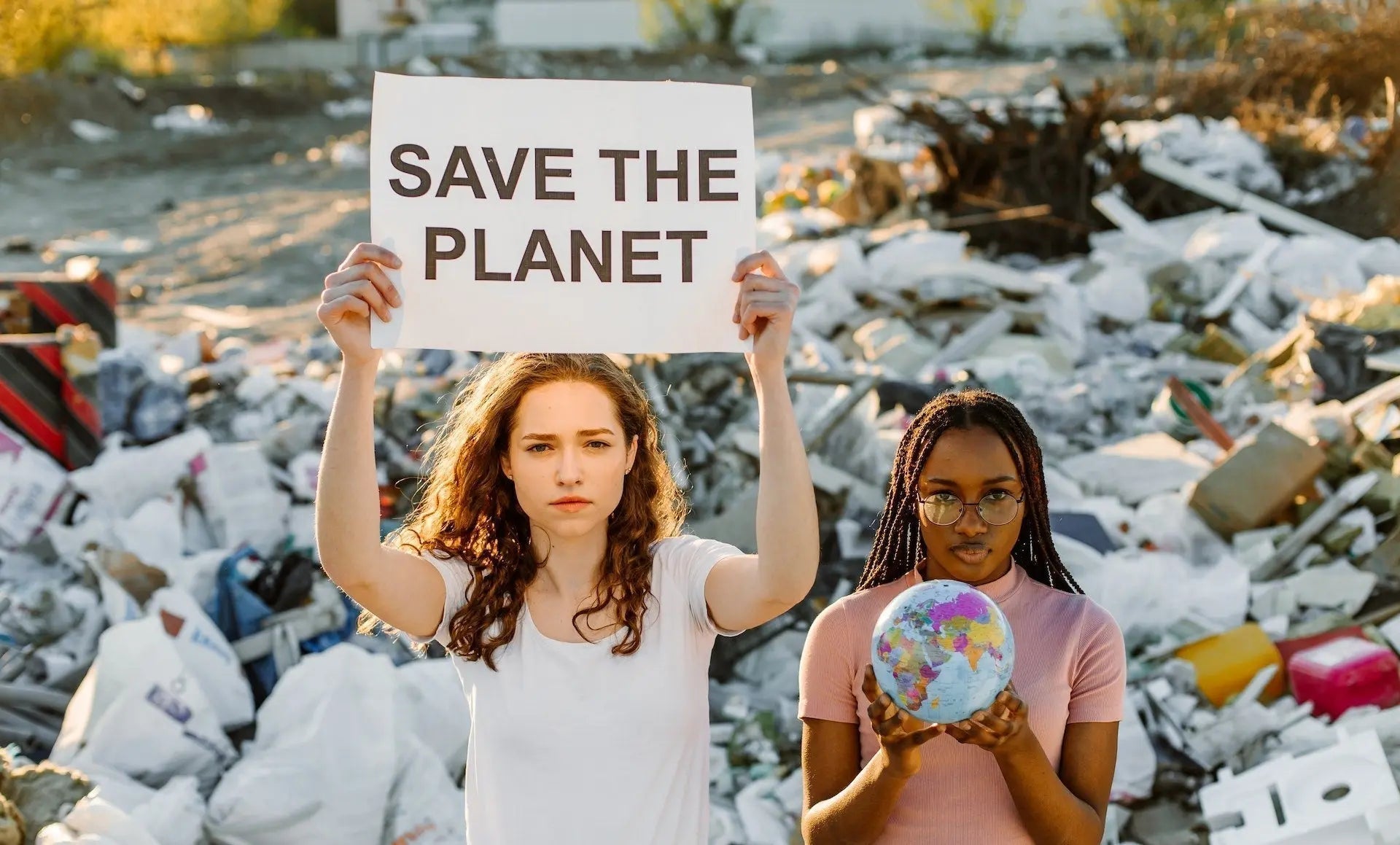 Two people holding signs about saving the planet in a landfill.