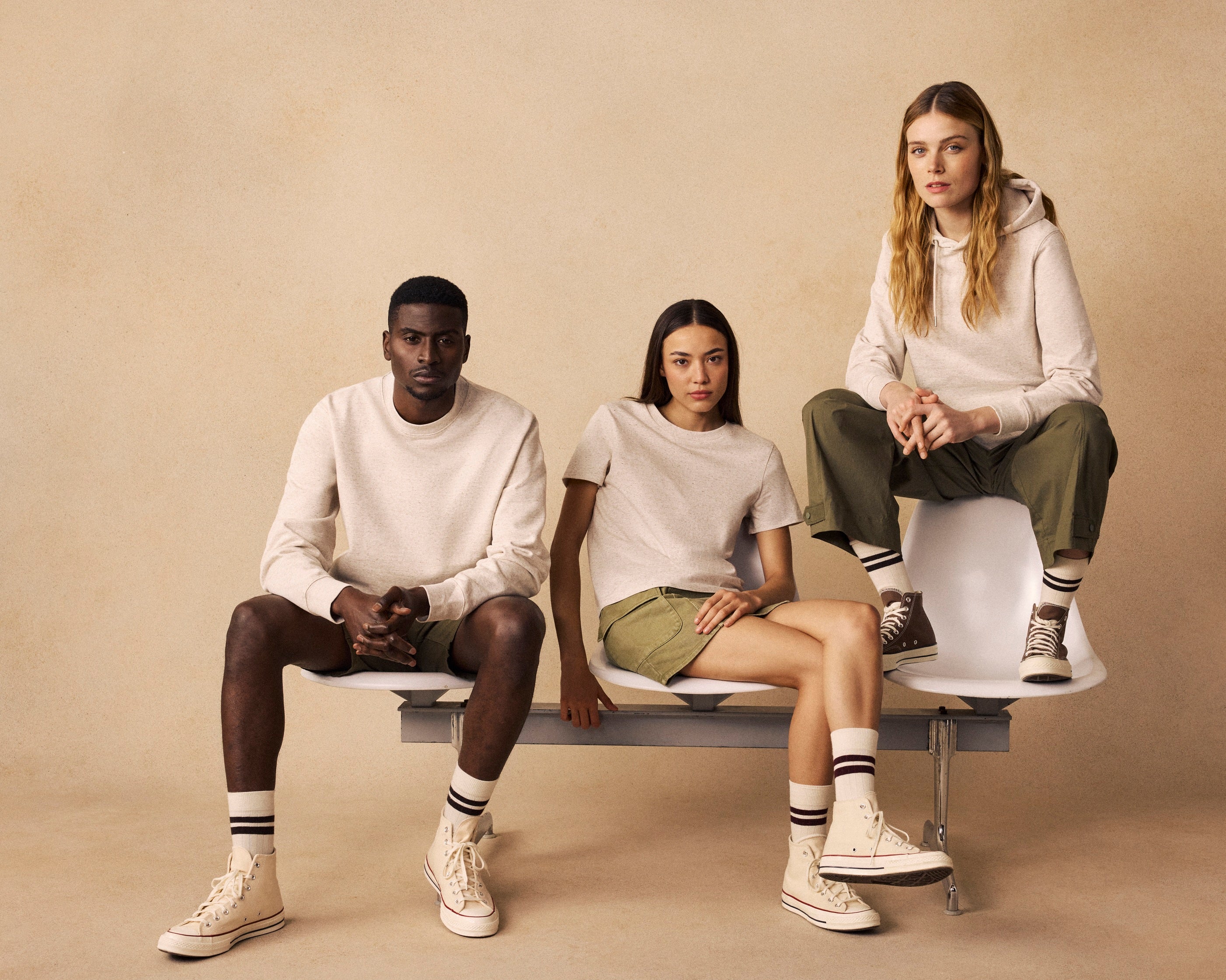 Three people sitting on a bench against a beige background