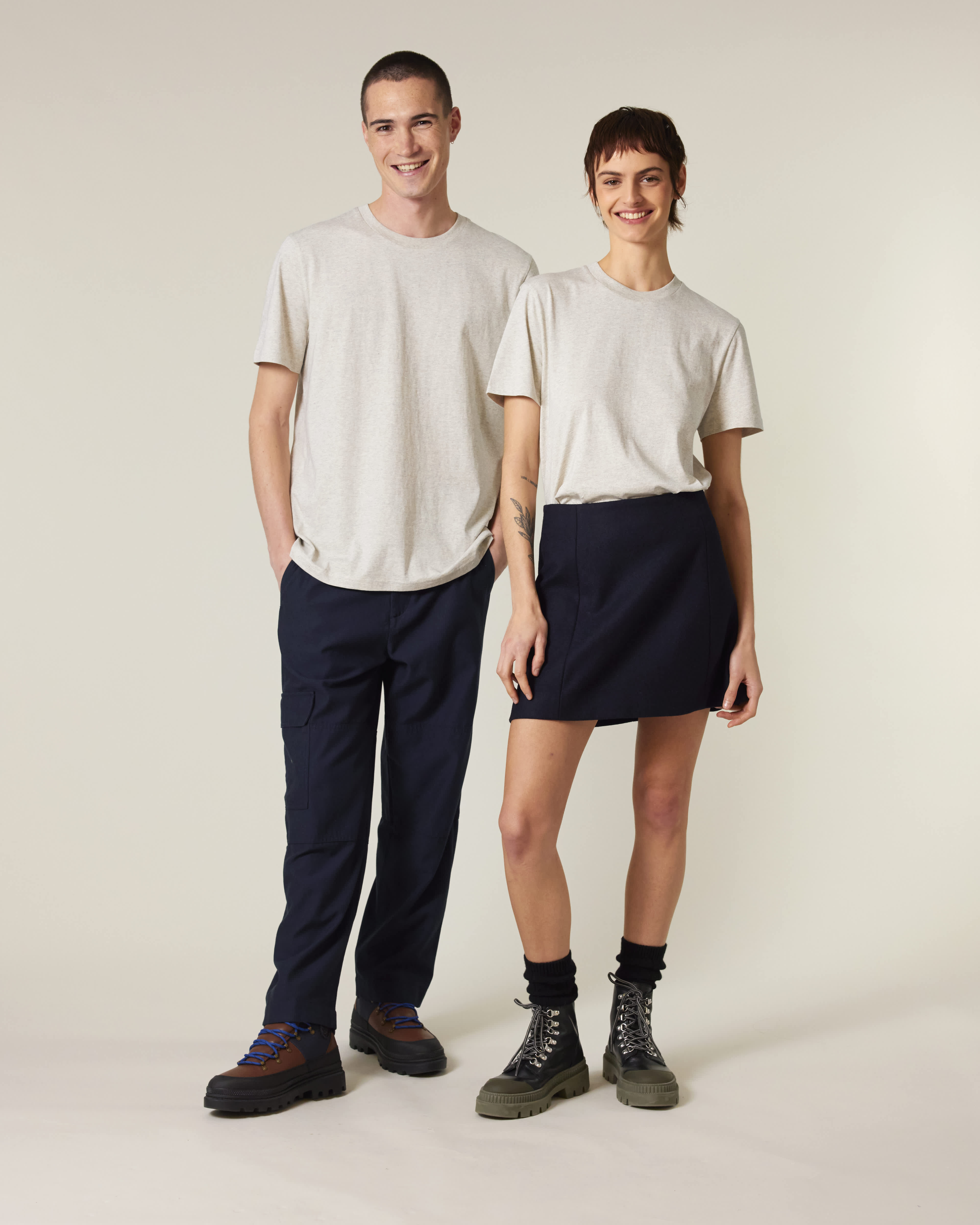 Two people wearing matching outfits with navy pants and white shirts on a plain background