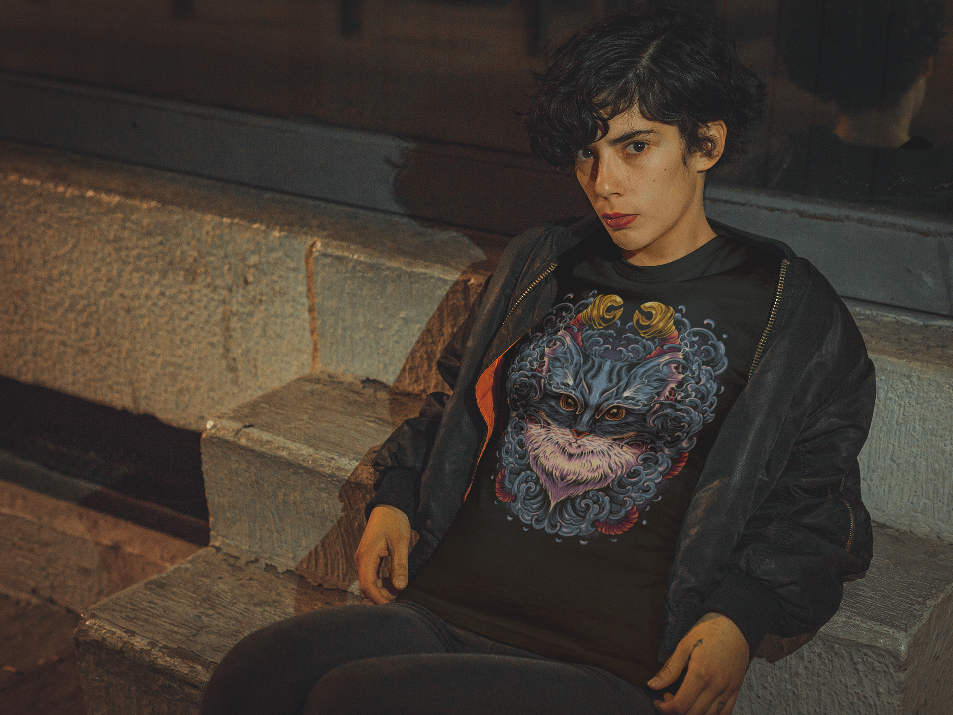 Person wearing a black T-shirt with a colorful TeeStitch Apparel exclusive graphic design, sitting on stone steps.