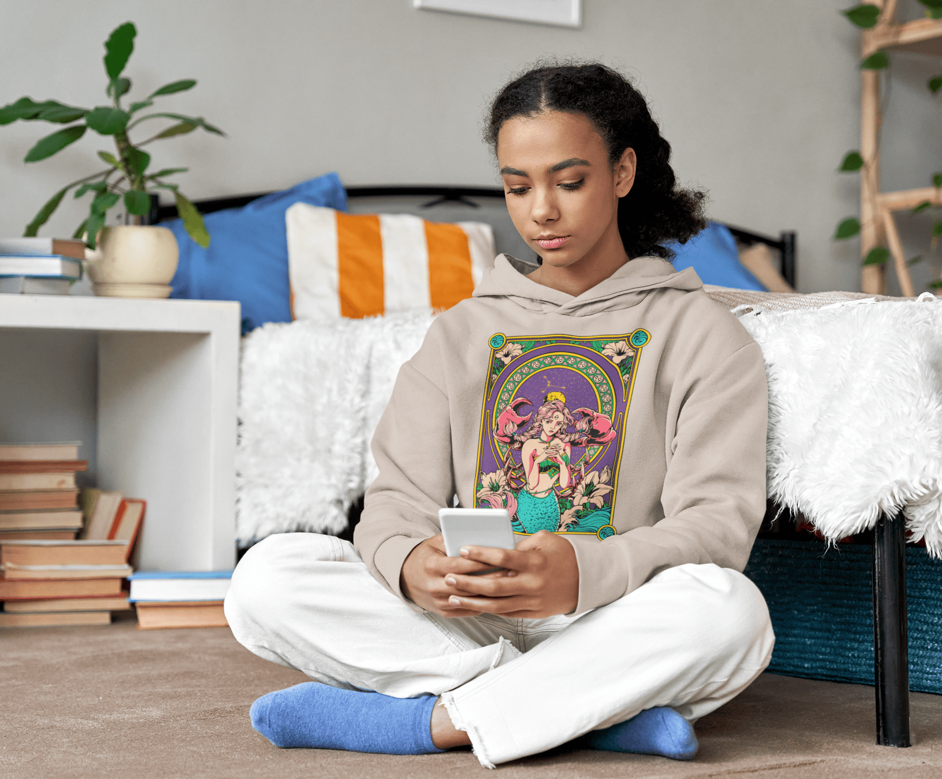 Person sitting on a couch wearing a hoodie with a colorful design, holding a phone.