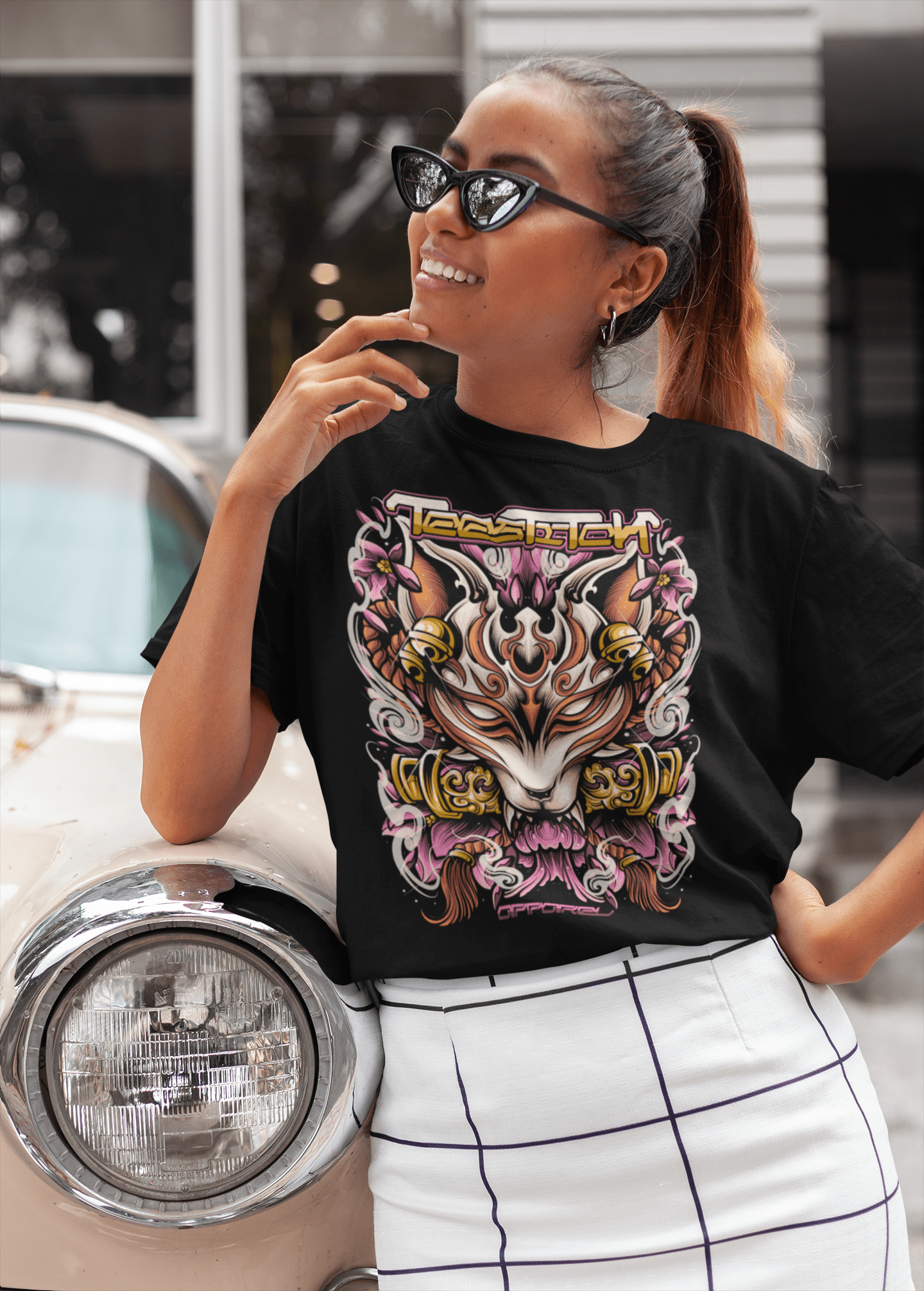 Woman wearing a black t-shirt with a colorful graphic design, standing next to a vintage car.