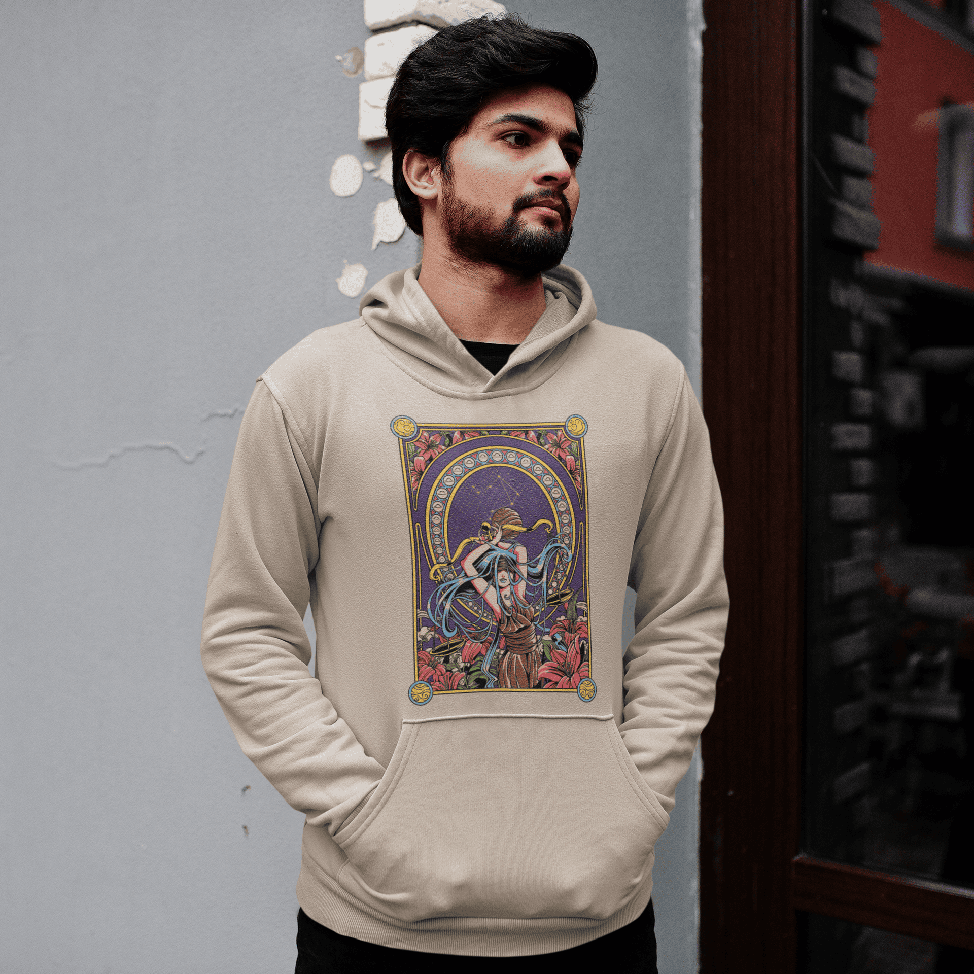 Man wearing a beige hoodie with a colorful graphic design on a gray wall.