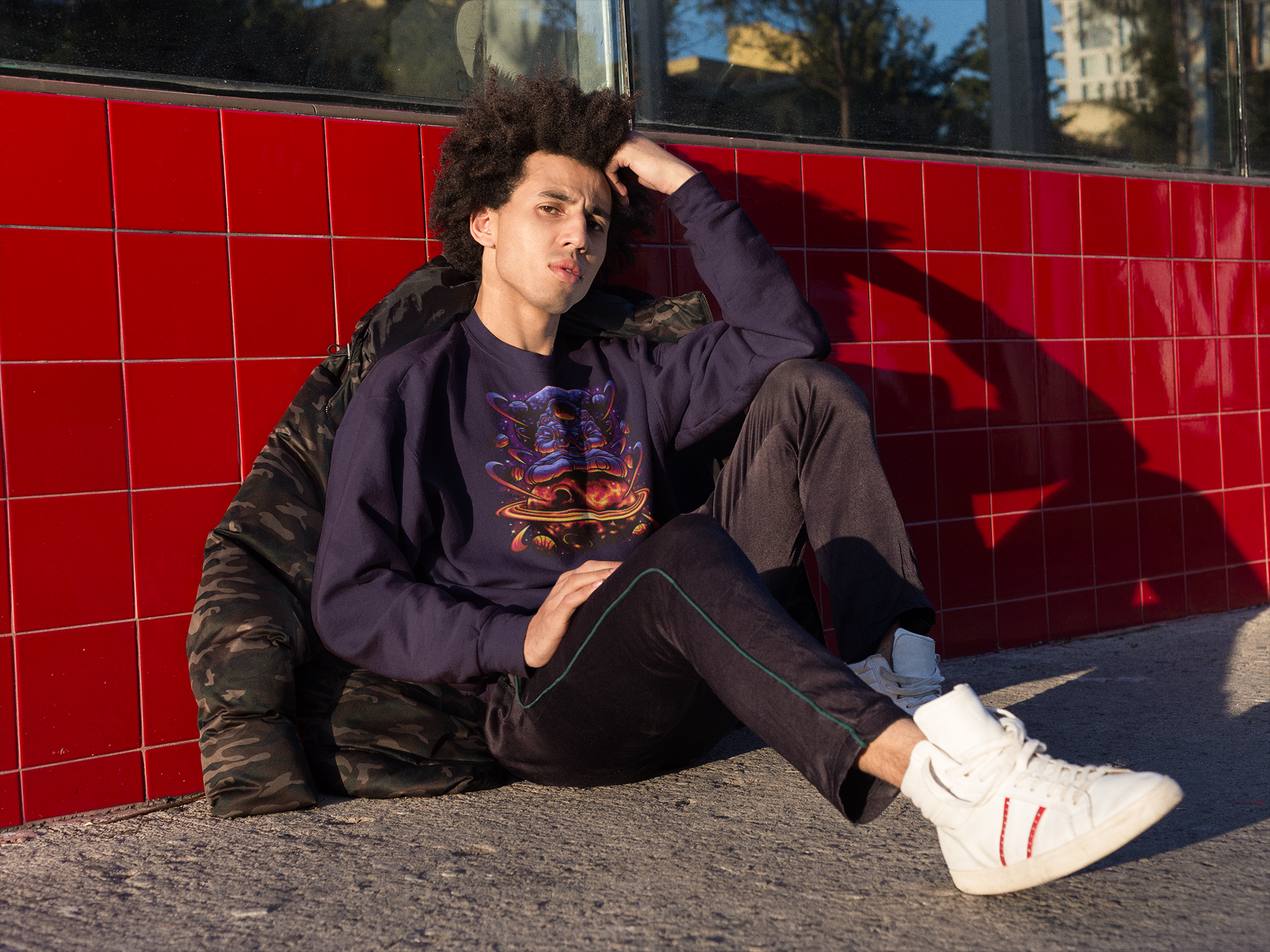 mockup-of-a-man-wearing-a-crewneck-sweatshirt-sitting-against-a-red-tiles-wall-TeeStitch-Apparel